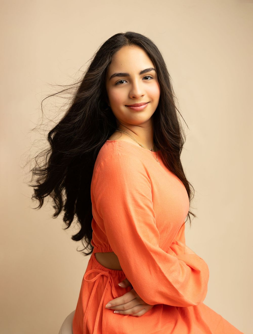 Portrait of someone in a vibrant coral dress with flowing dark hair against a neutral backdrop.