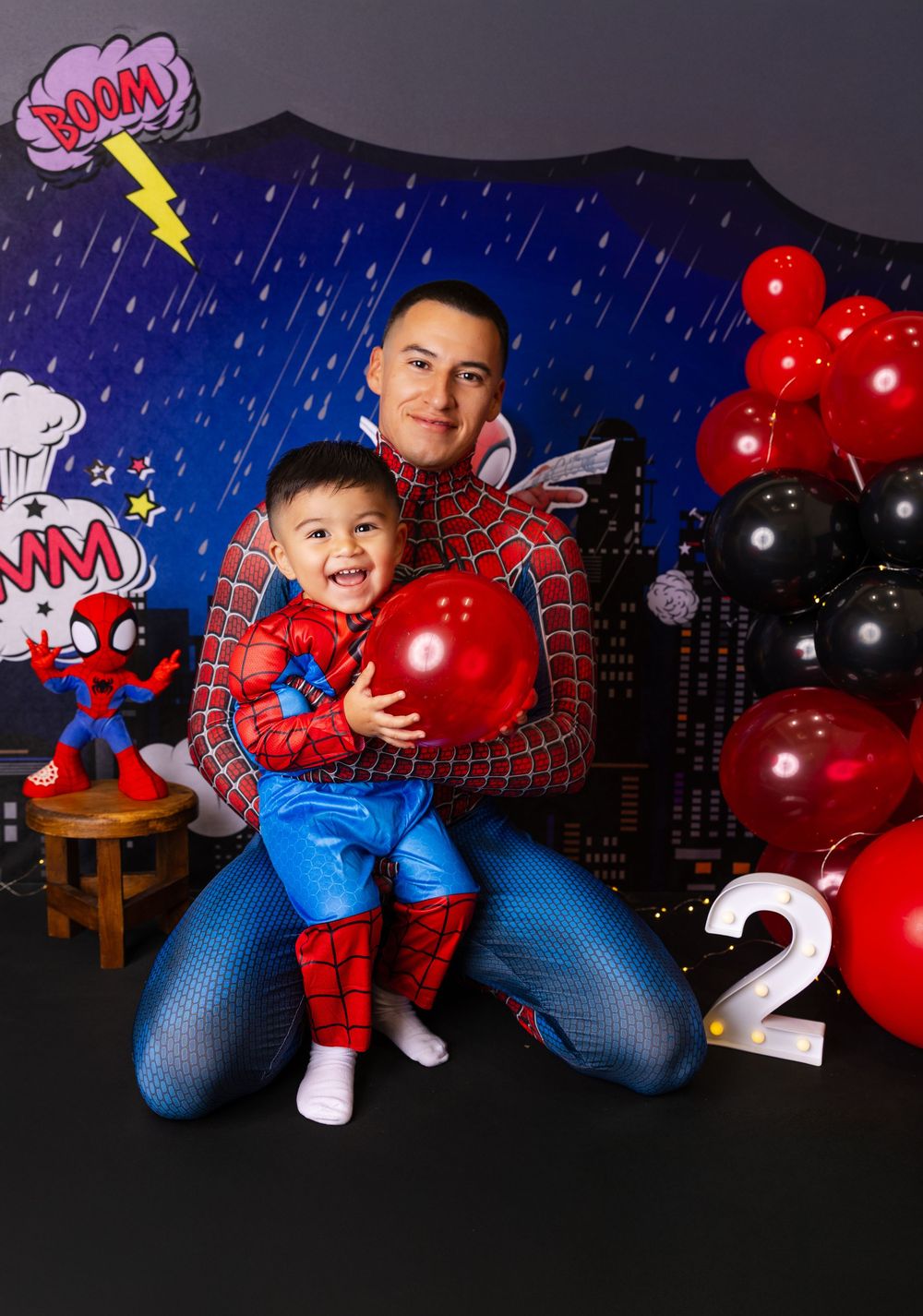 A Spider-Man themed photo session with red and black balloons against a dark cityscape backdrop.