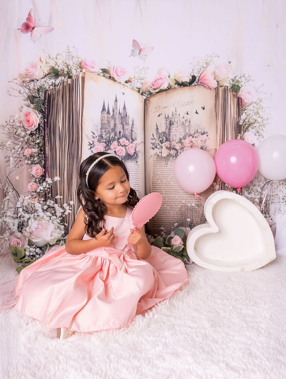 Pink and white themed photo session setup with balloons, floral arrangements, and a cozy bed against a textured backdrop.