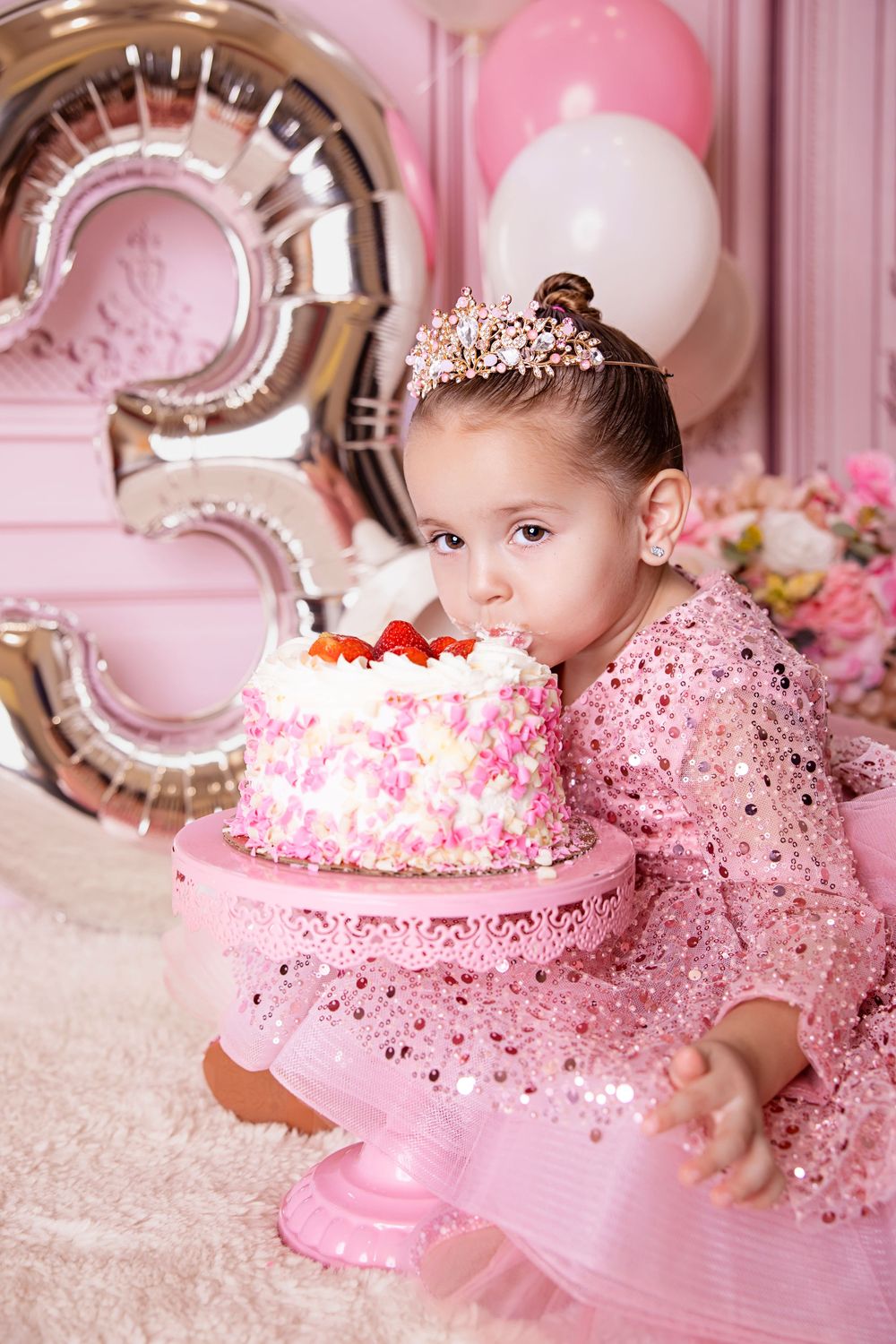 Pink glittery first birthday cake smash photo session with sparkly tulle dress and silver balloon decorations.