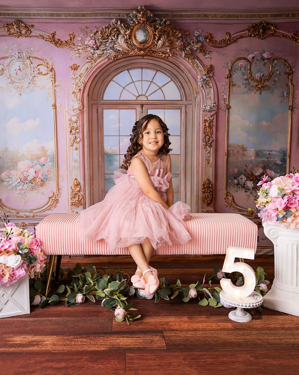 A pink and gold decorated room with ornate French-style panels and floral accents creates an elegant backdrop for a birthday setup.