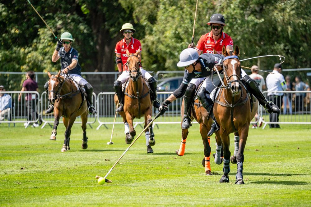 Polo players in action during match swinging mallets at ball on grass field.