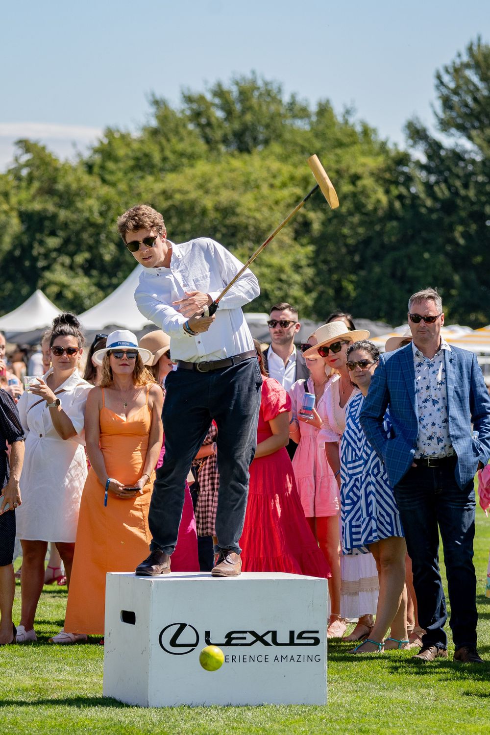 Person swinging mallet while standing on Lexus branded platform during polo event.
