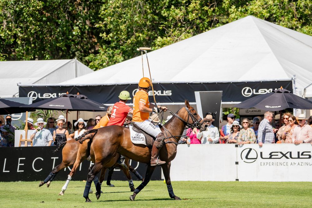 Polo player riding at full gallop past Lexus branded tents during tournament match.