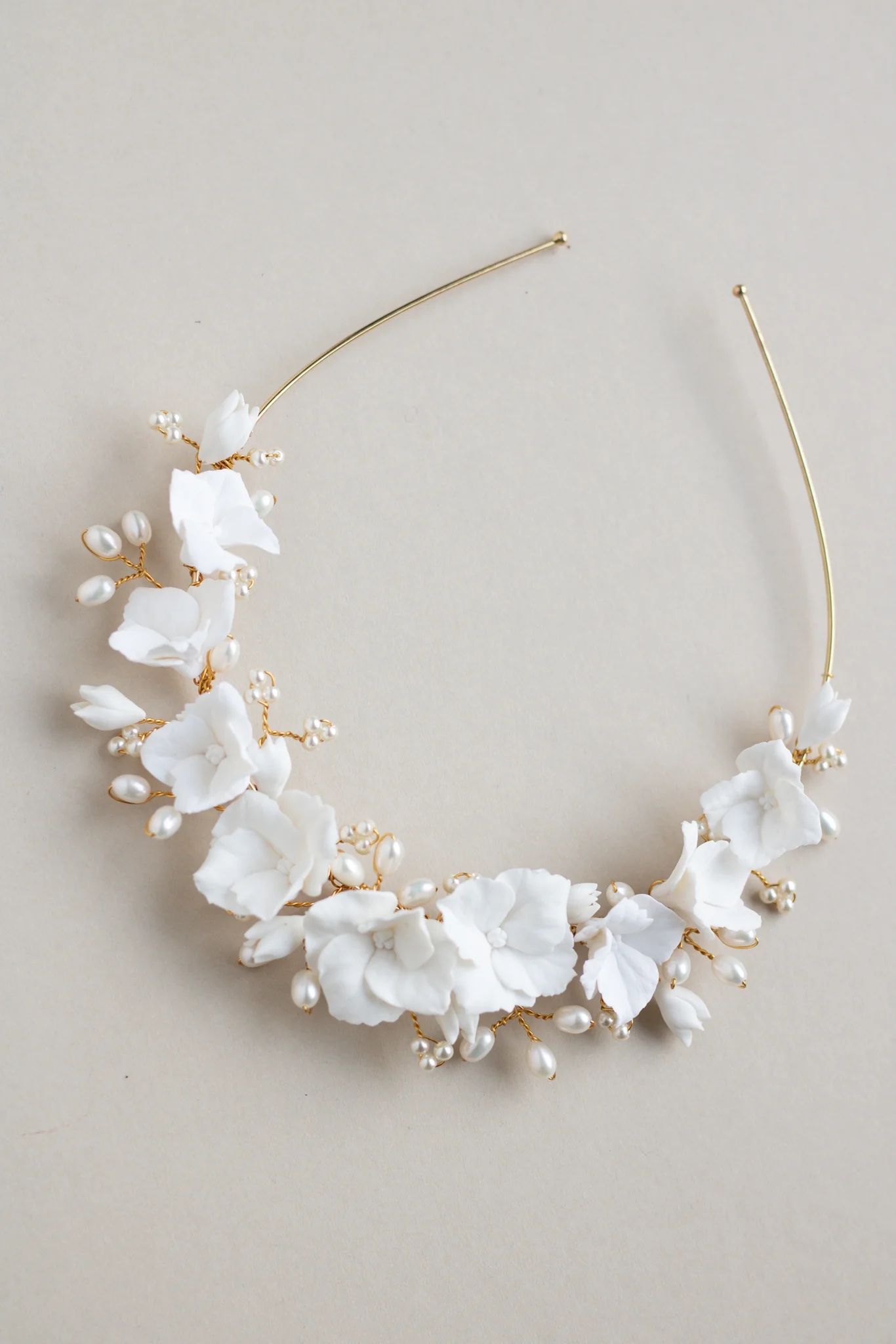 Ornate bridal headpiece featuring white flowers and pearls on gold wire against neutral background.