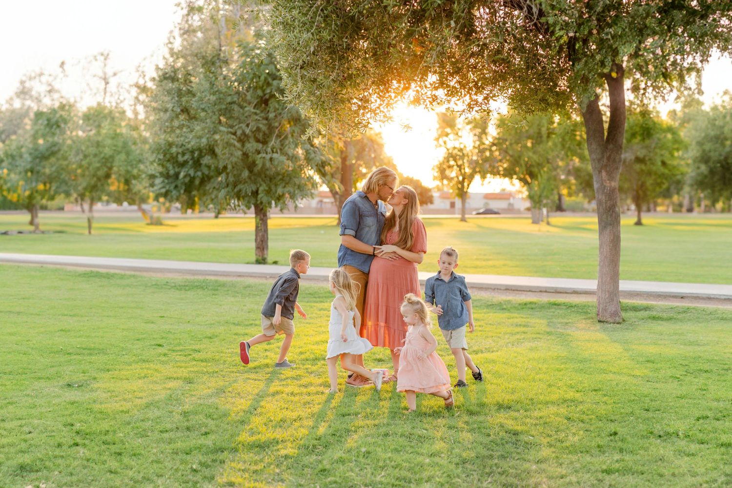 A family enjoys quality time together by a white fence with golden autumn foliage in the background.