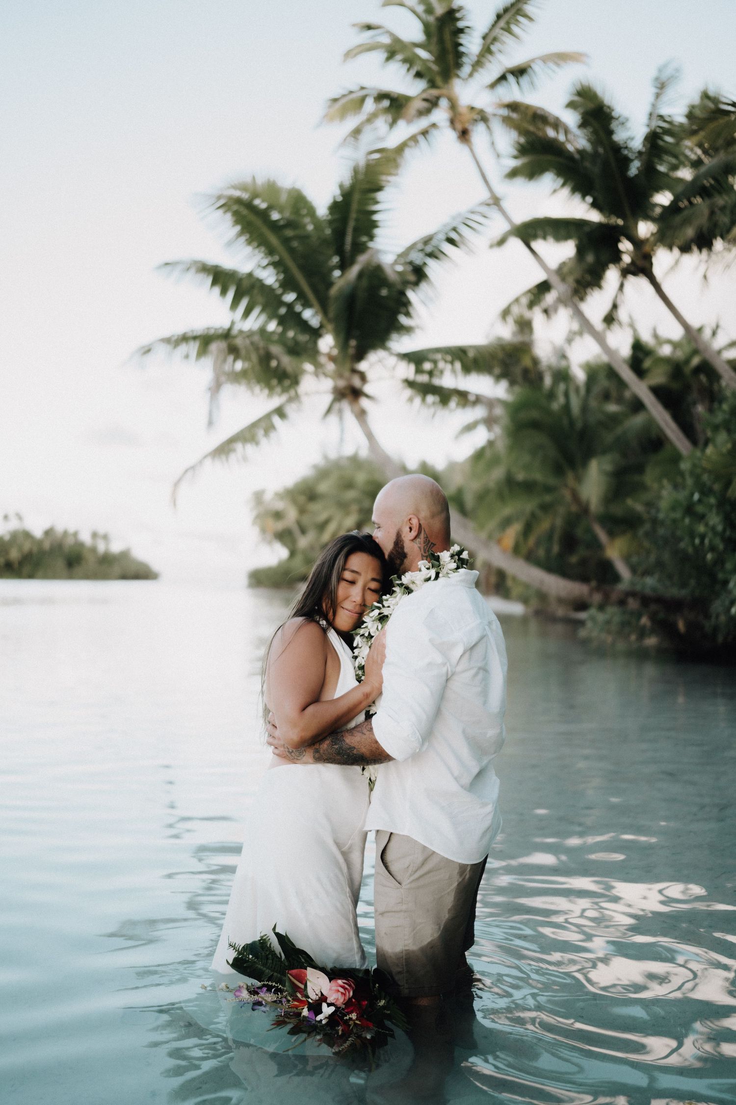 A romantic beach wedding scene with a flowing white veil and tropical palm trees silhouetted against bright sunlight.