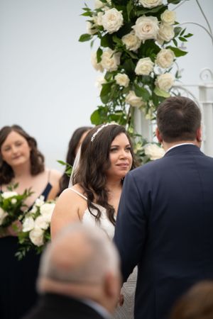 Wedding ceremony setup with white rose floral arch and guests in attendance.