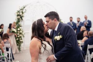 A couple shares their first kiss under a floral arch during their wedding ceremony.