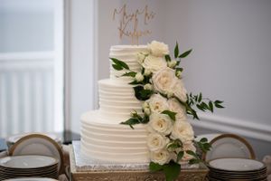 White wedding cake decorated with fresh roses and a gold topper.