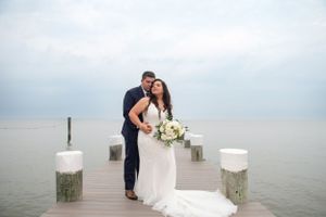 Newlyweds posing on a wooden pier over misty water with white lanterns.
