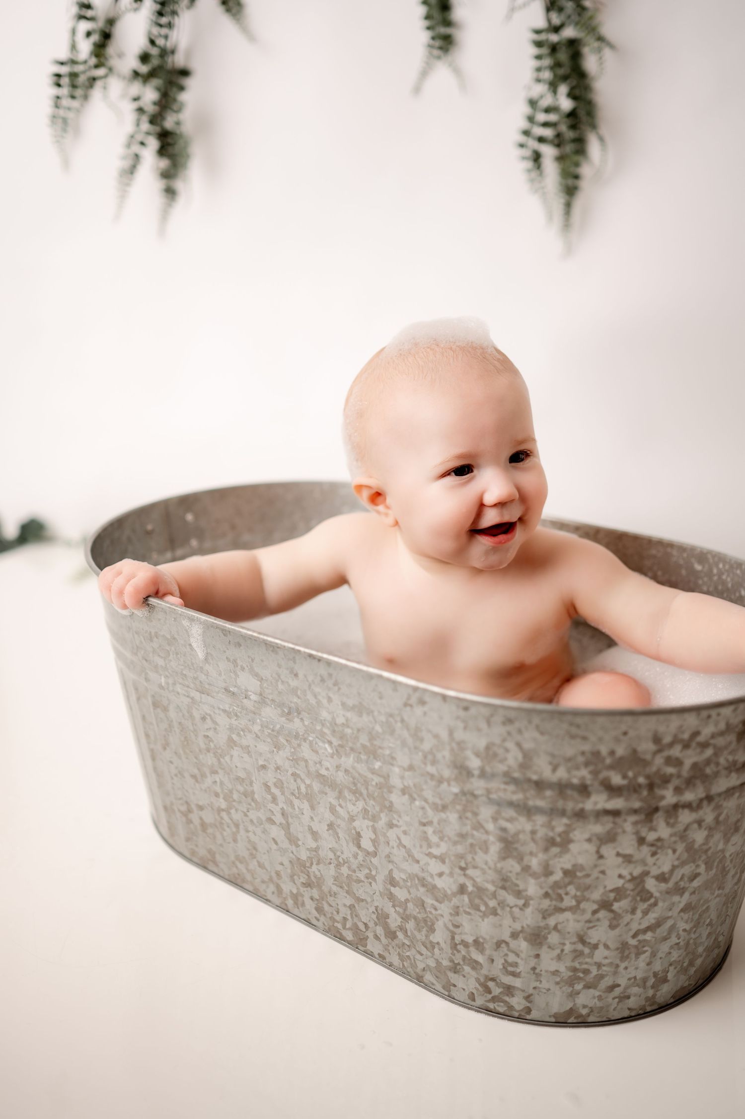 Bath time portrait in vintage metal tub with hanging greenery decoration.