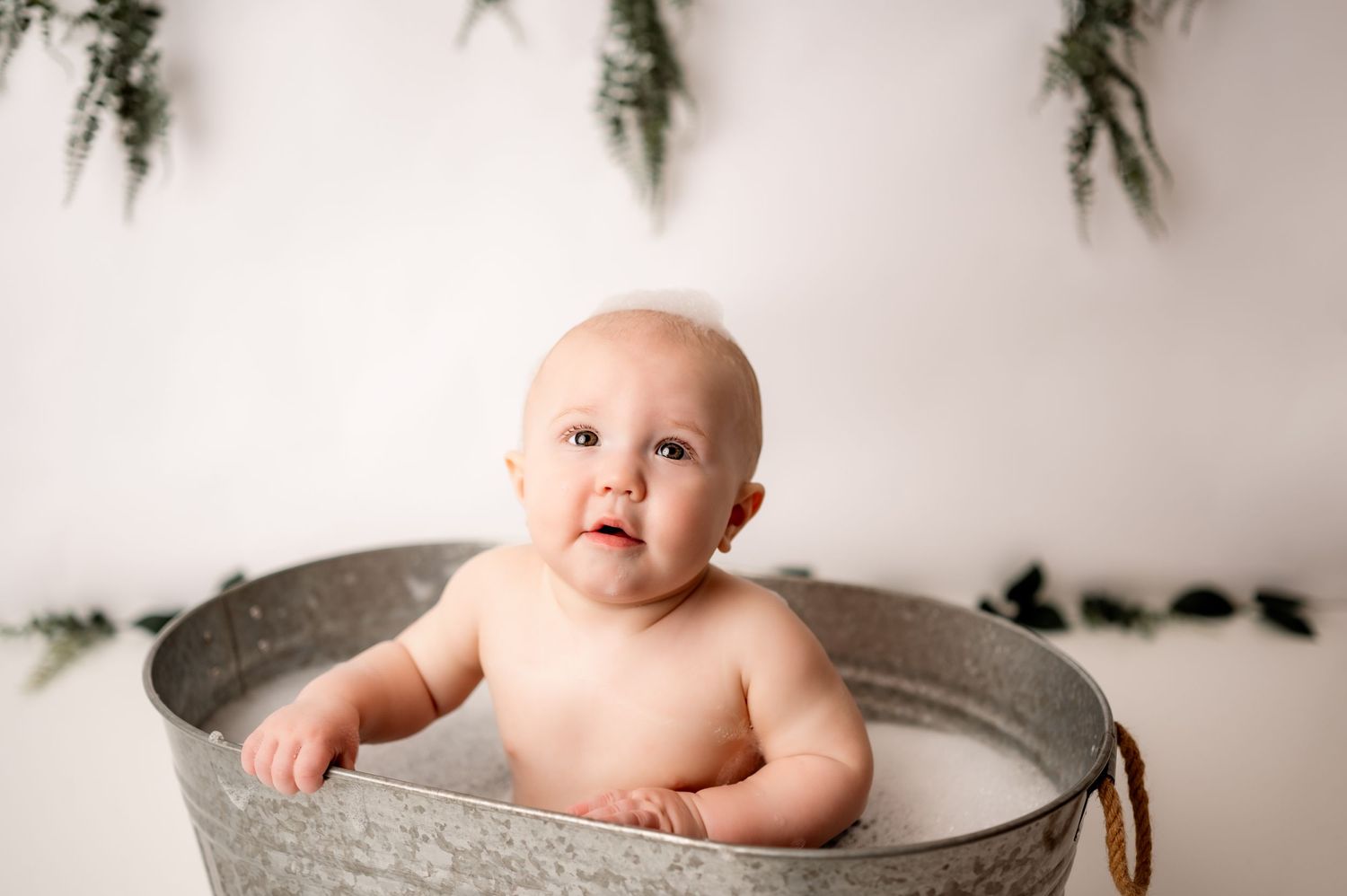 Sweet bath time portrait in vintage metal tub against white backdrop with greenery.