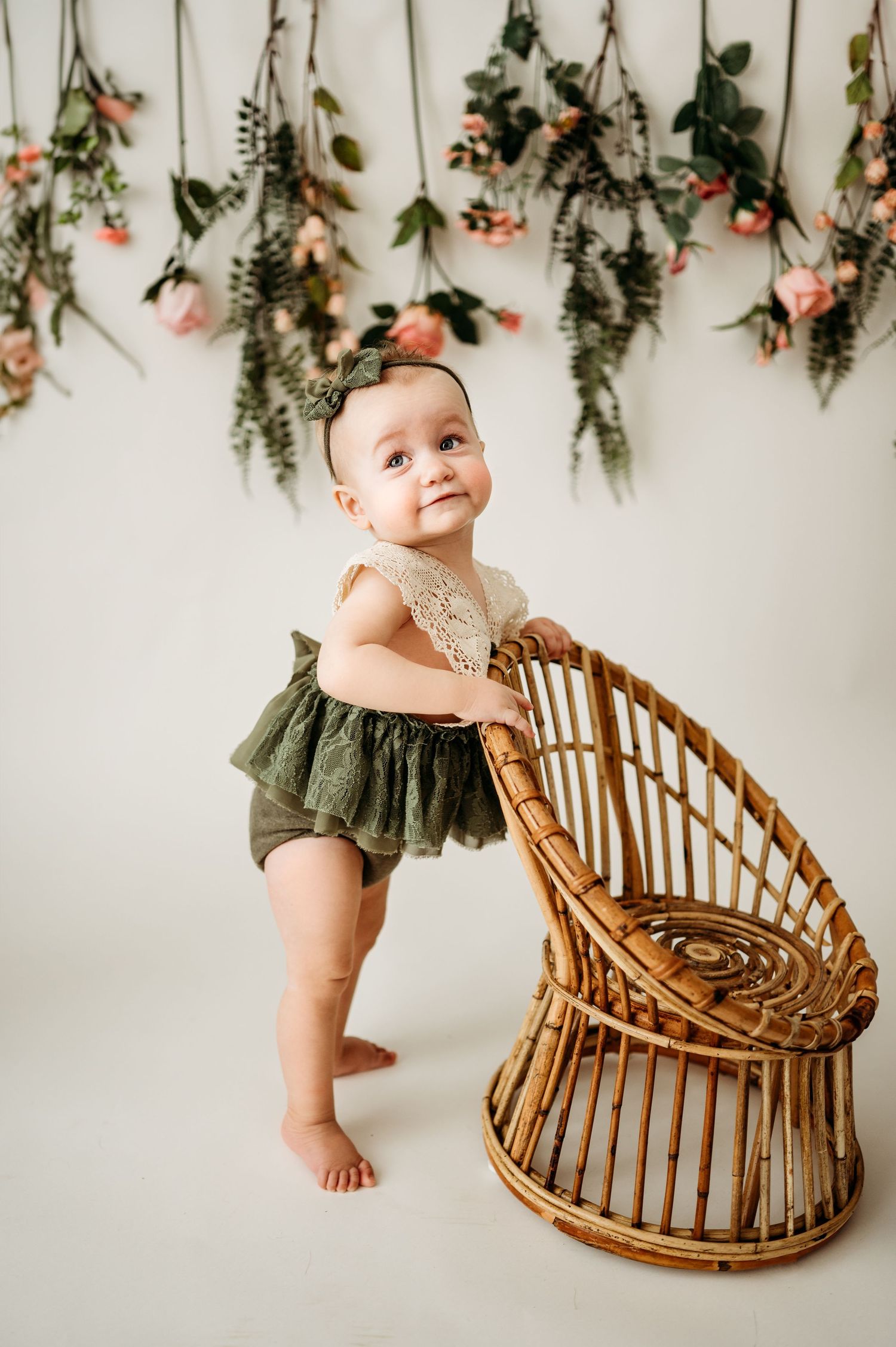 Studio portrait with rattan chair and hanging botanical decorations against white wall.
