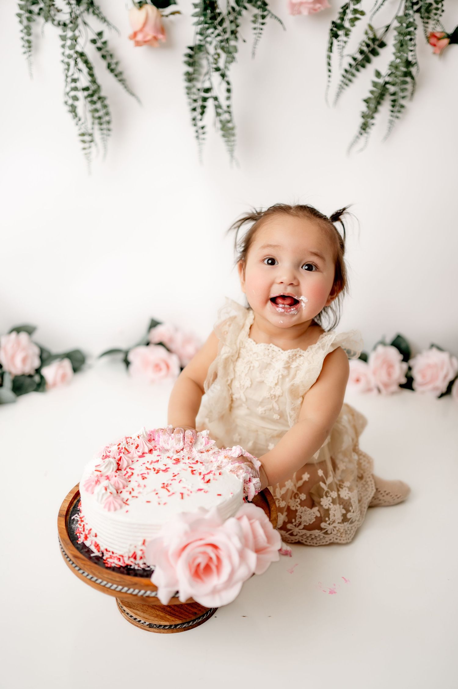 First birthday cake smash session with pink floral decorations and hanging greenery.