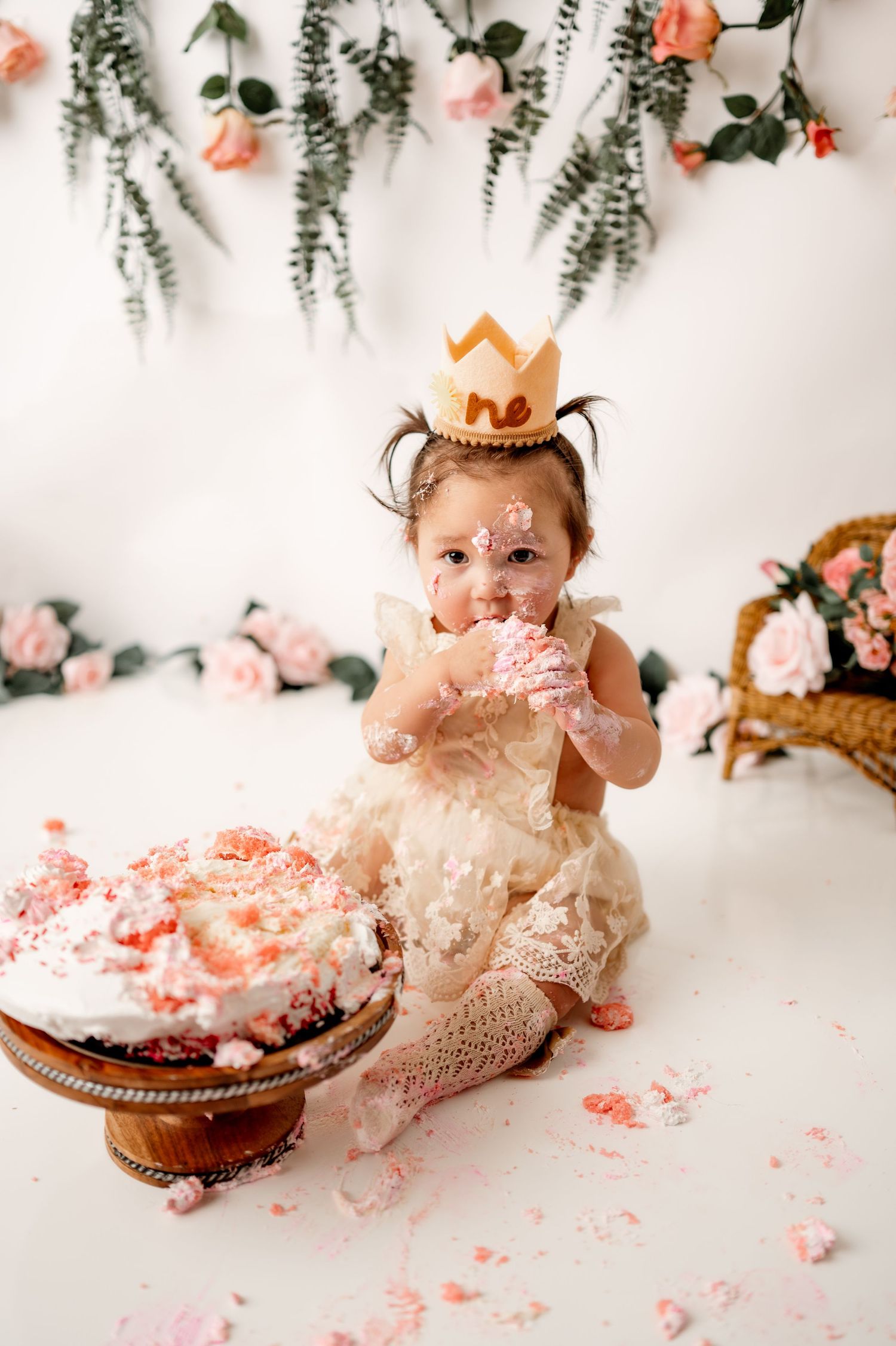 Baby wearing crown and lace dress enjoys messy cake smash photo session.