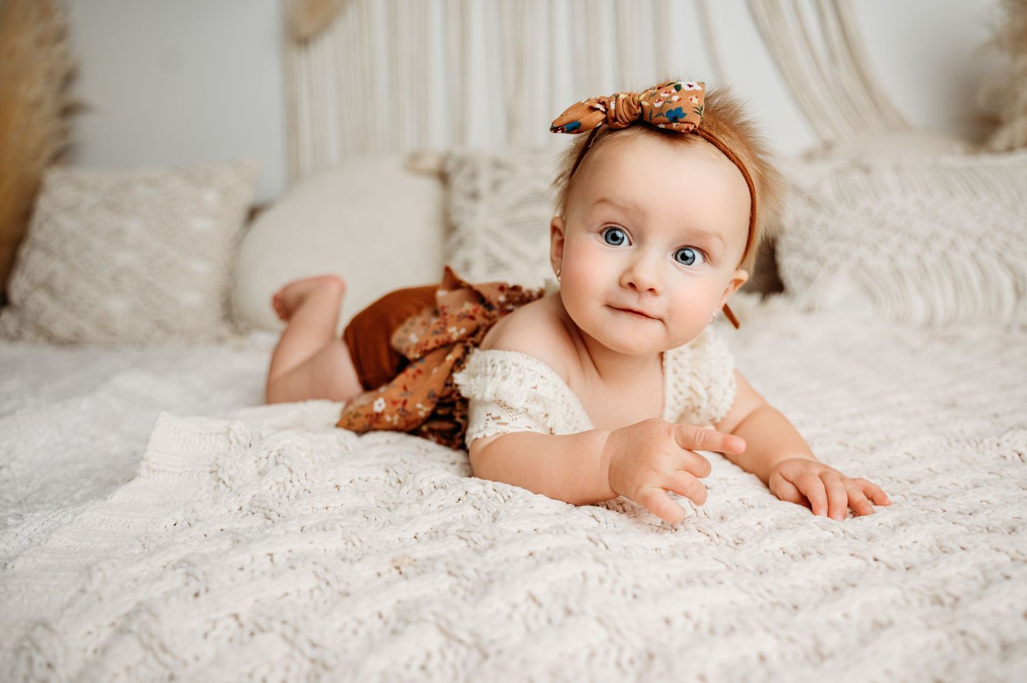 Baby in lace outfit with bow accessory lying on textured white bedding.