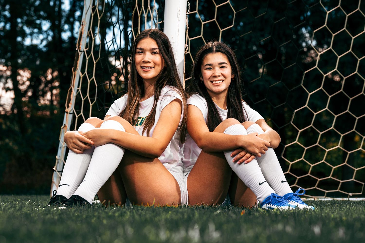 Two sisters from Roosevelt High School pose in their soccer uniforms against a soccer goal on a grassy field.