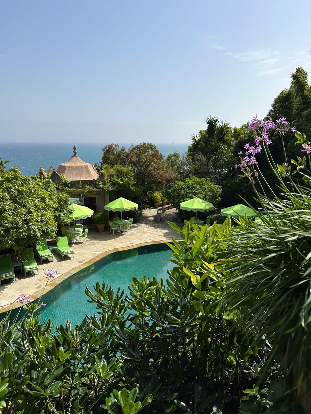 Tropical pool overlooking the ocean with bright green umbrellas and a thatched gazebo.