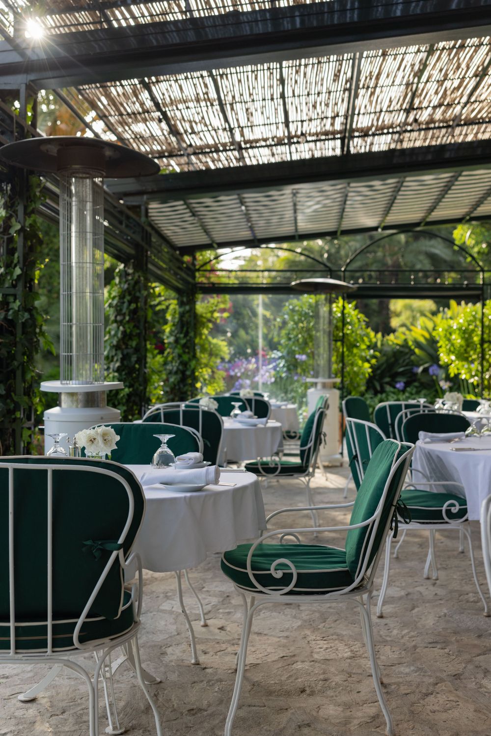 Elegant outdoor dining area with green cushioned chairs under a latticed pergola covered in vines.