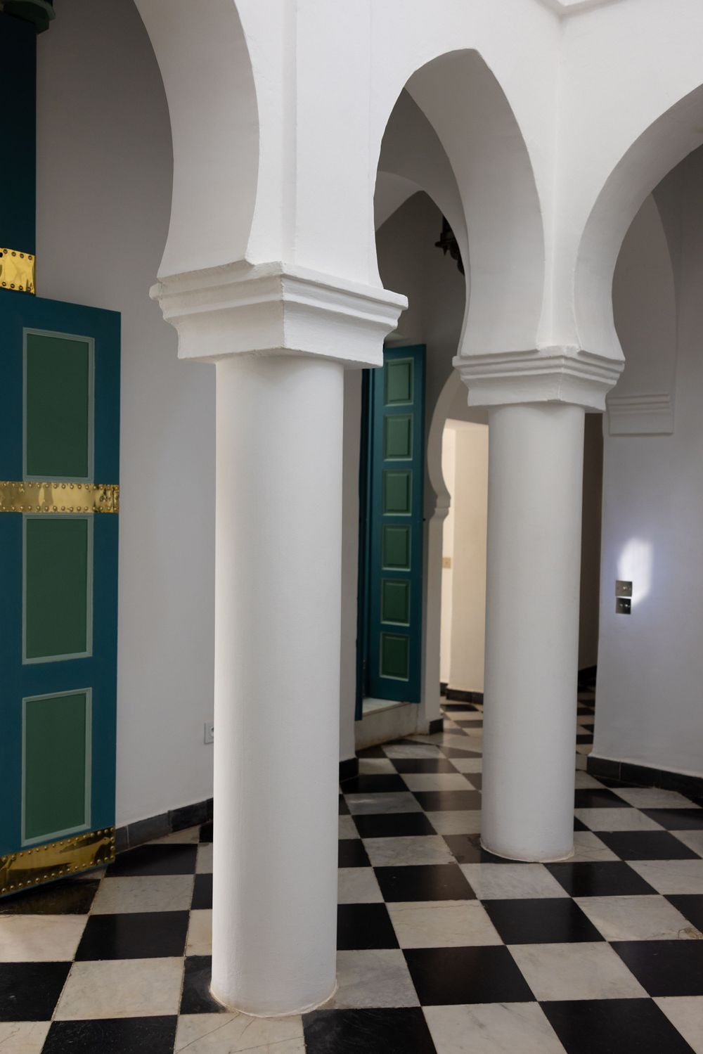 Interior hallway with classic white columns, green doors, and black and white checkered flooring.
