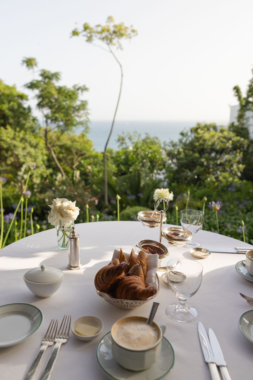 Elegant breakfast table setting with bread basket, coffee cups and ocean view.