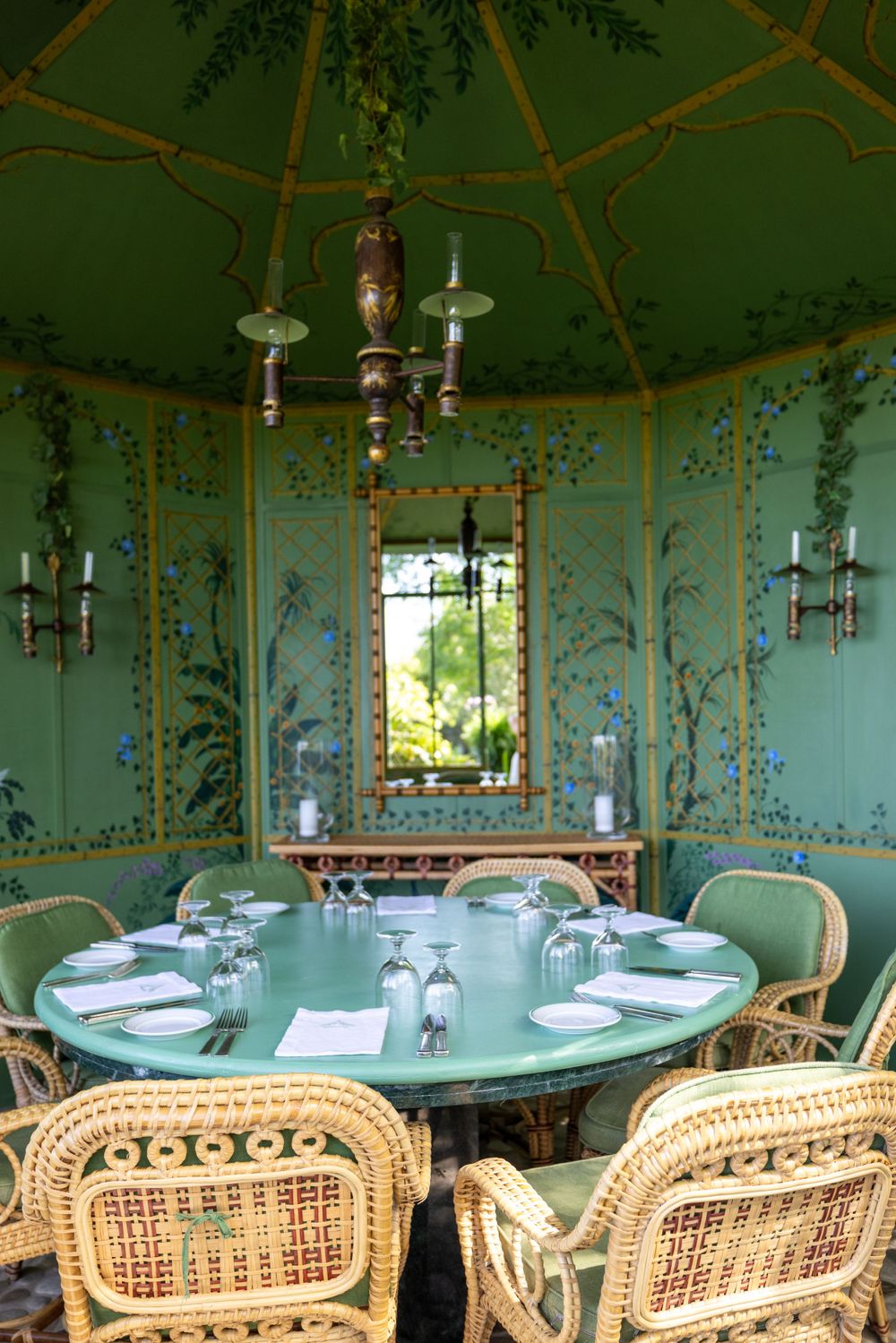 Elegant dining room with mint green walls decorated with floral murals and rattan chairs.