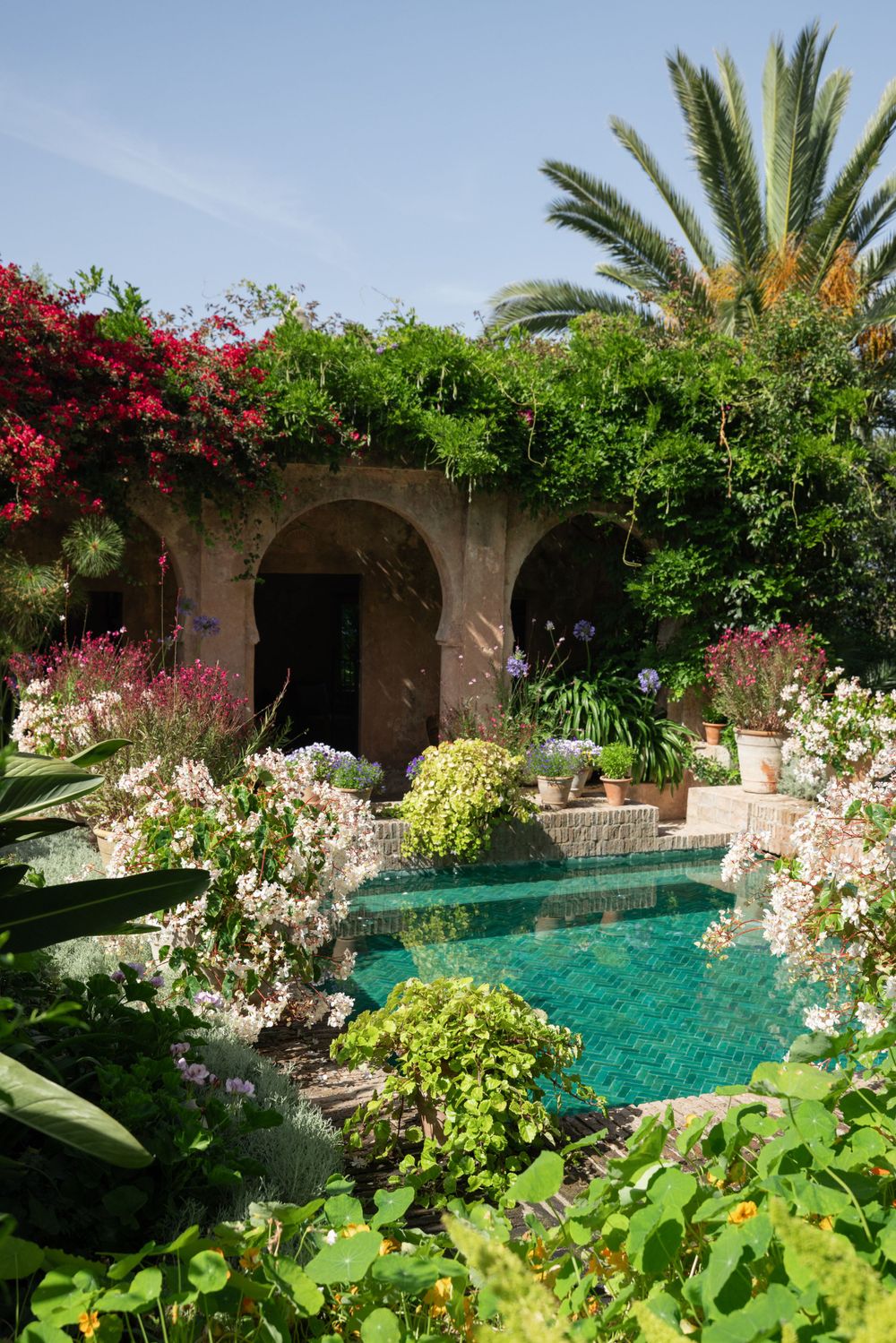 Luxurious Mediterranean garden pool surrounded by stone arches and flowering plants.