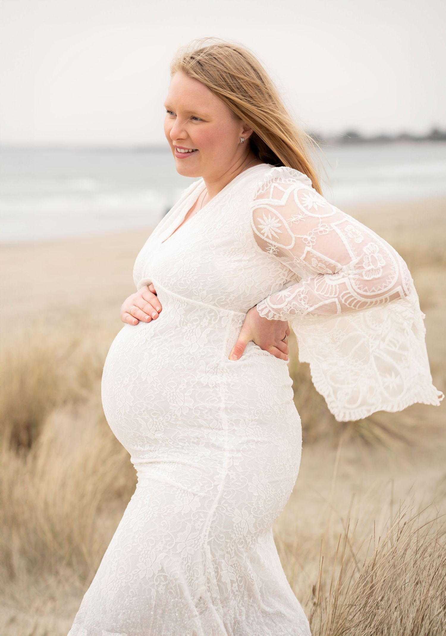 Gravidfotografering på Solastranden, smilende gravid kvinne i hvit kjole.