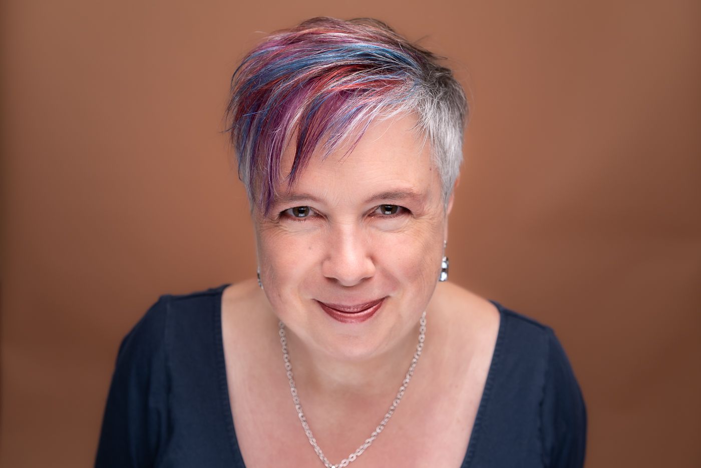 Studio headshot of a woman with colourful hair.
