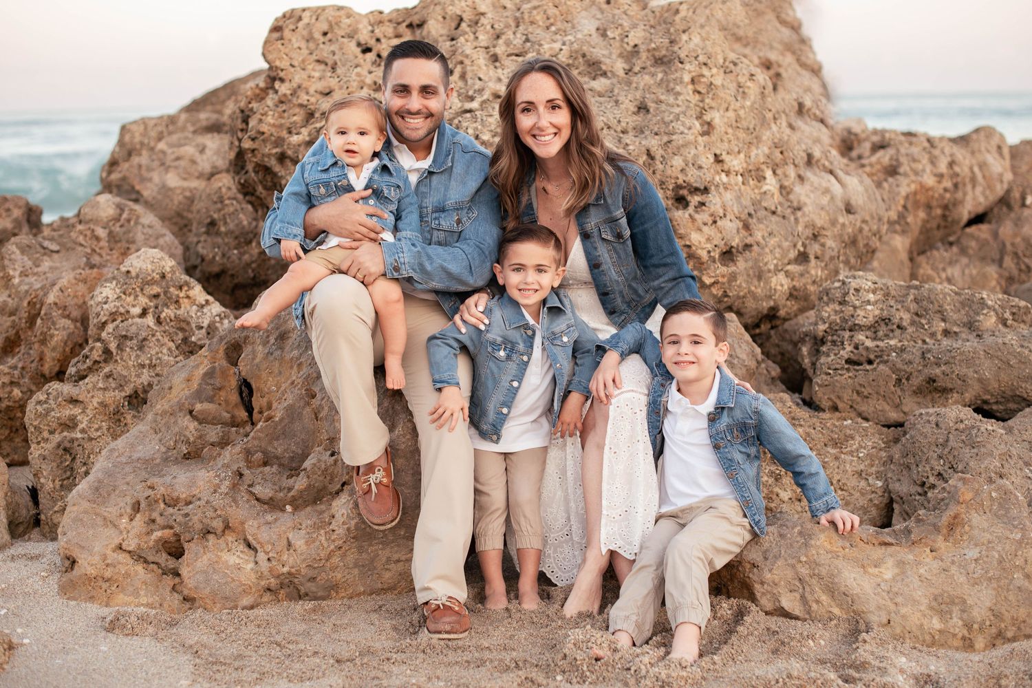 Happy family of five poses together on rocky beach during golden hour.