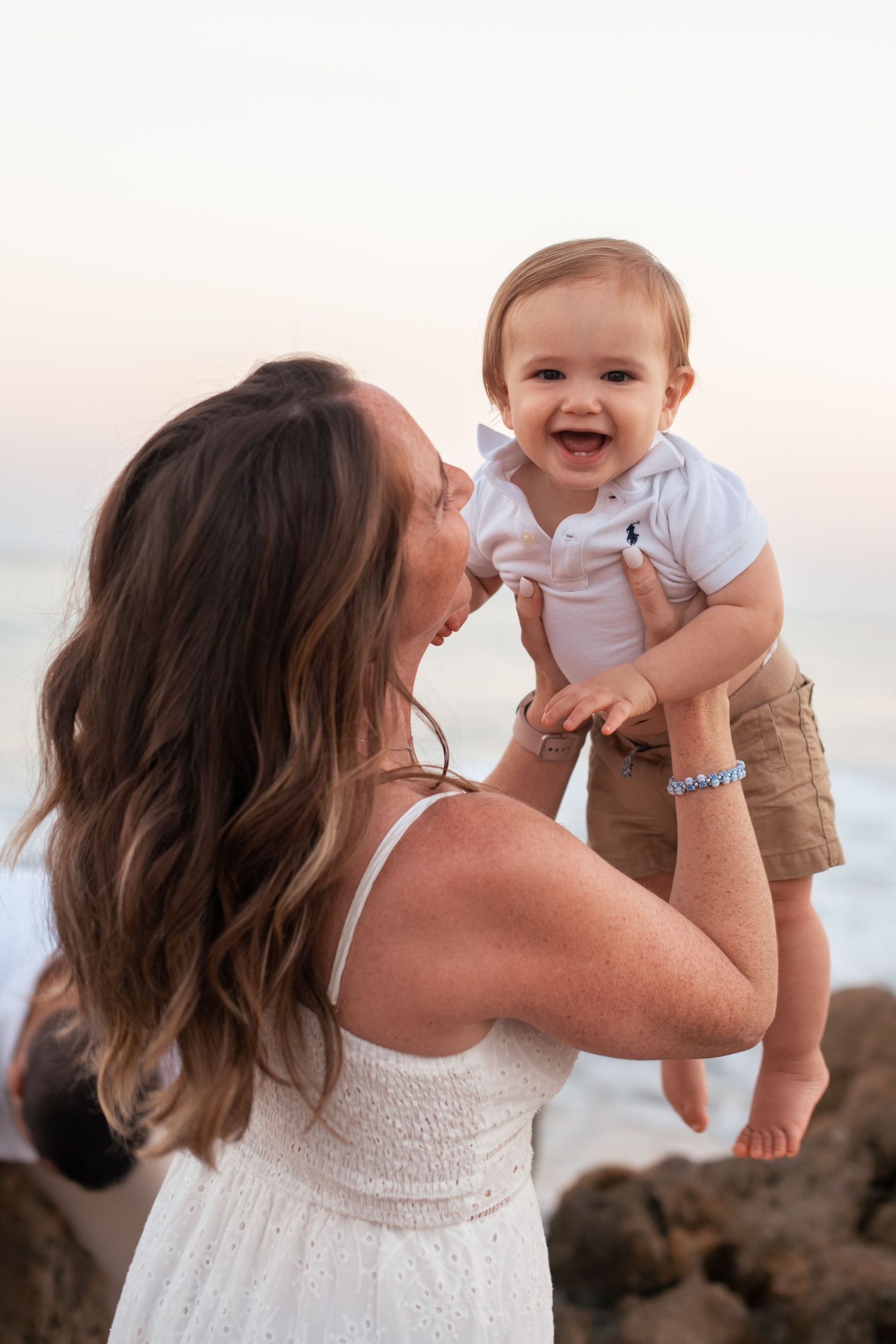 Mother and baby share joyful moment together on beach at sunset.