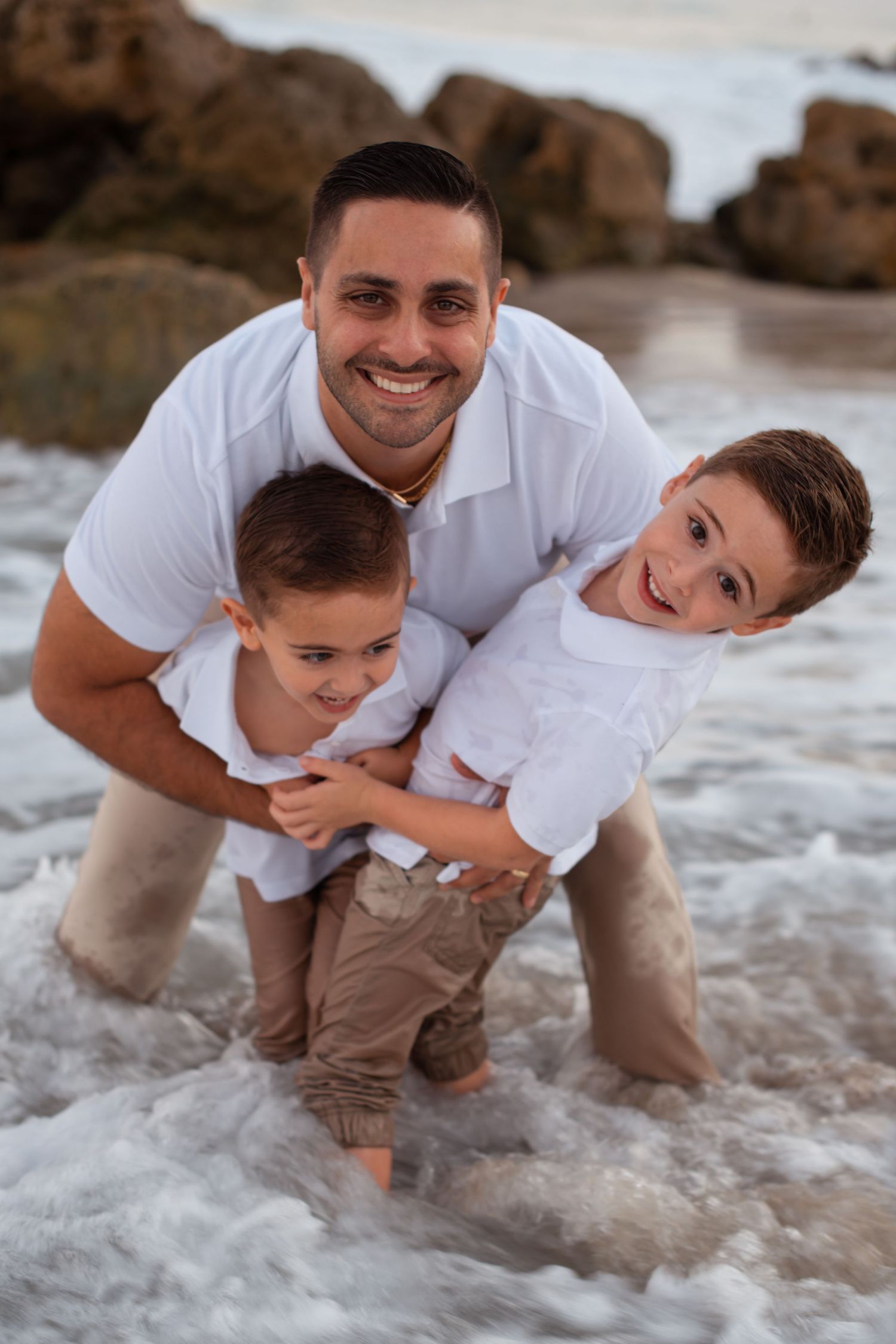 Father and children play in ocean waves during beach sunset photoshoot.