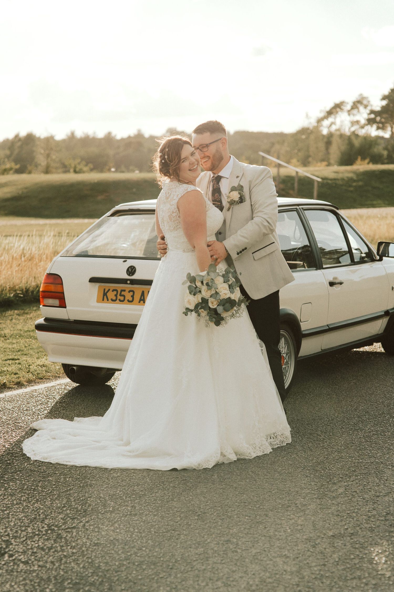 Newlyweds pose with vintage white car for romantic wedding photographs.