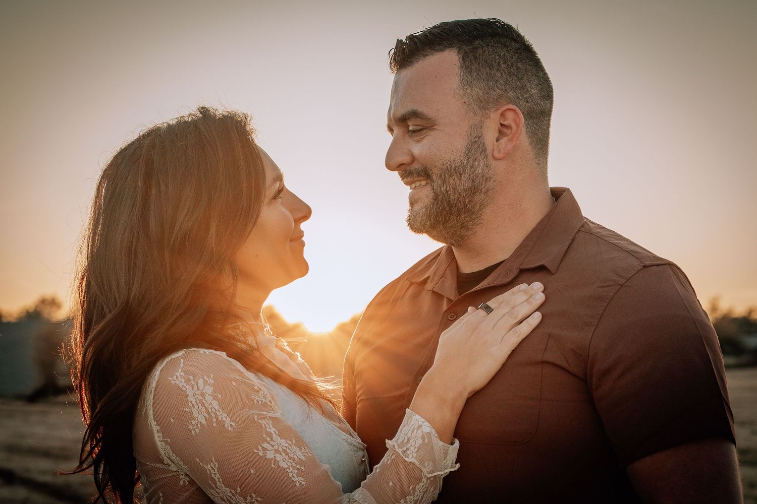 A couple shares a romantic moment together during golden hour sunset, with the woman wearing a white lace dress.