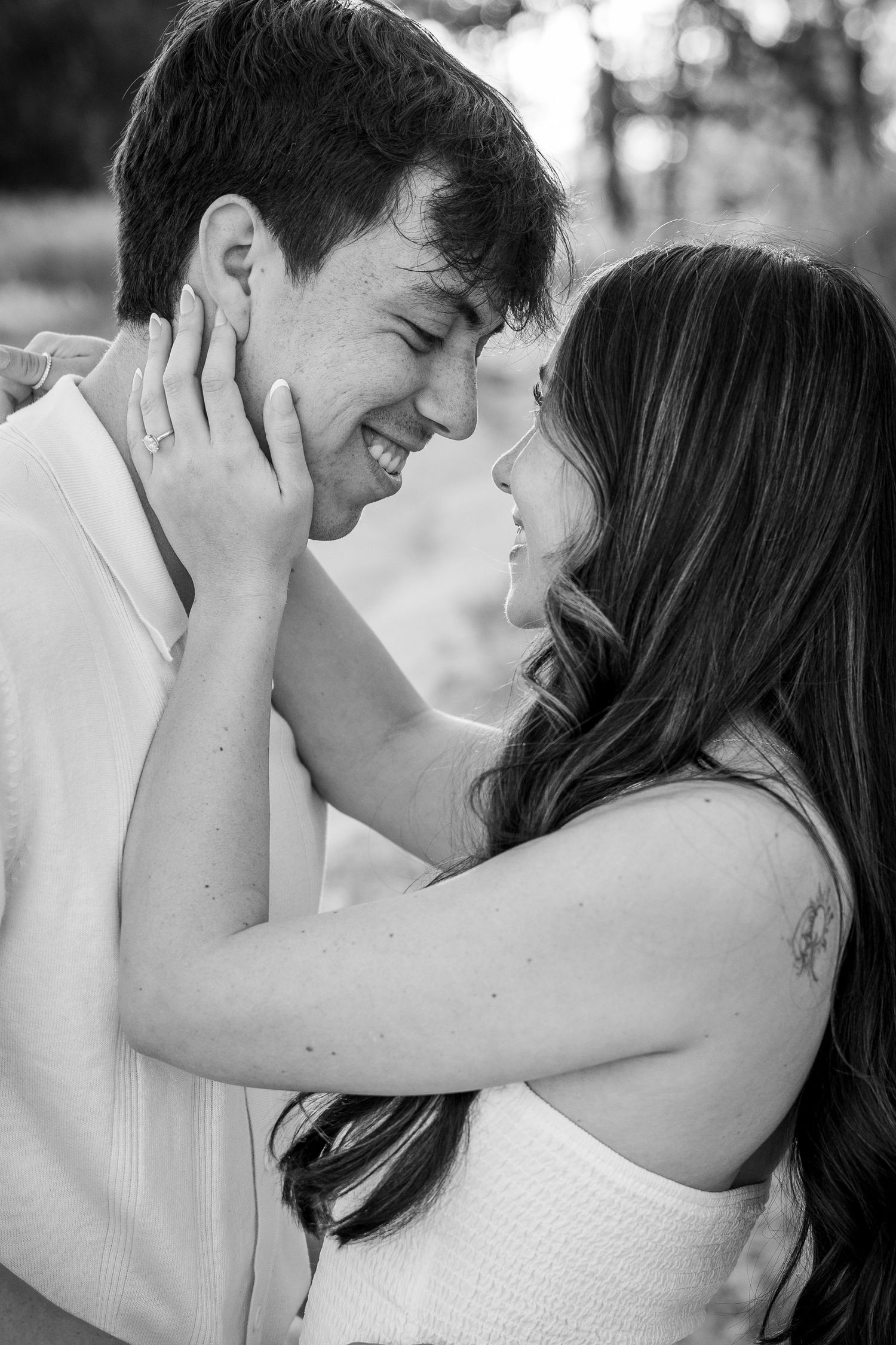 Black and white photo of a smiling couple sharing a tender moment, foreheads touching, woman gently holding mans face.