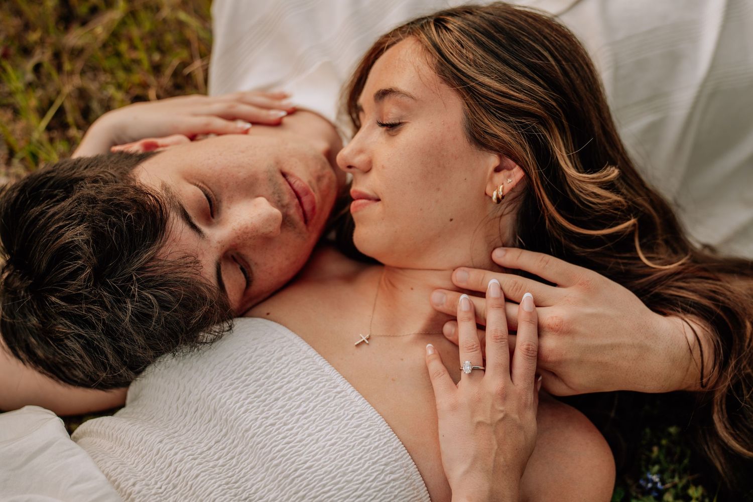 Romantic couple lying together outdoors, eyes closed, sharing a tender intimate moment on a white blanket.