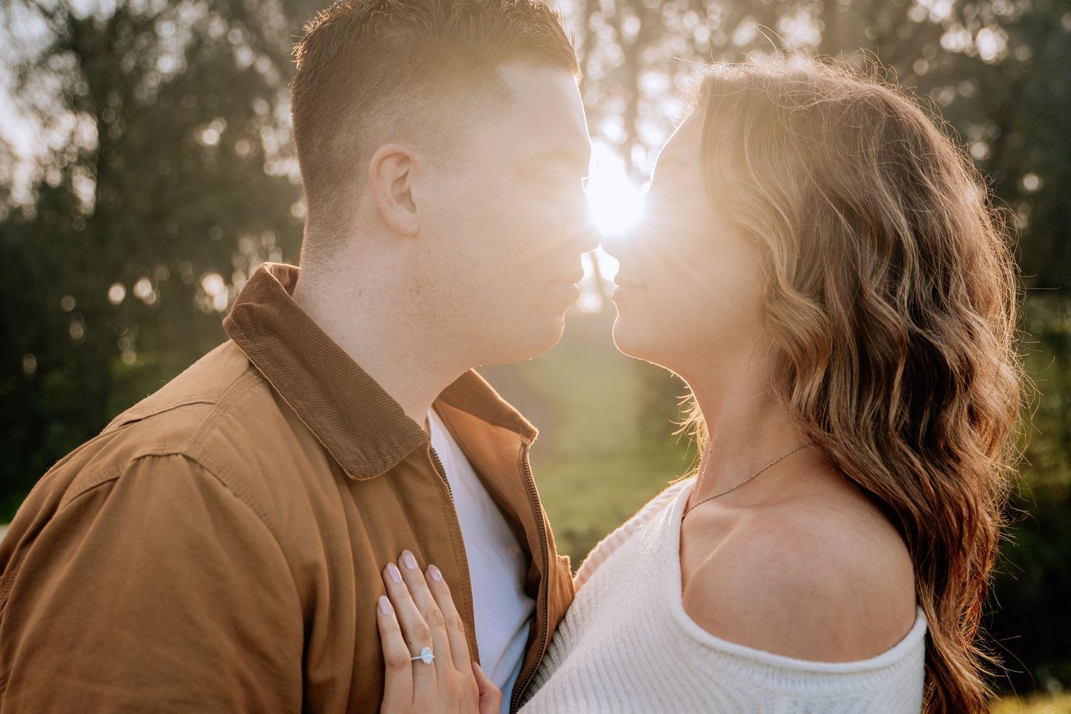 A couple shares a tender moment in golden sunlight filtering through trees during a romantic outdoor photoshoot.