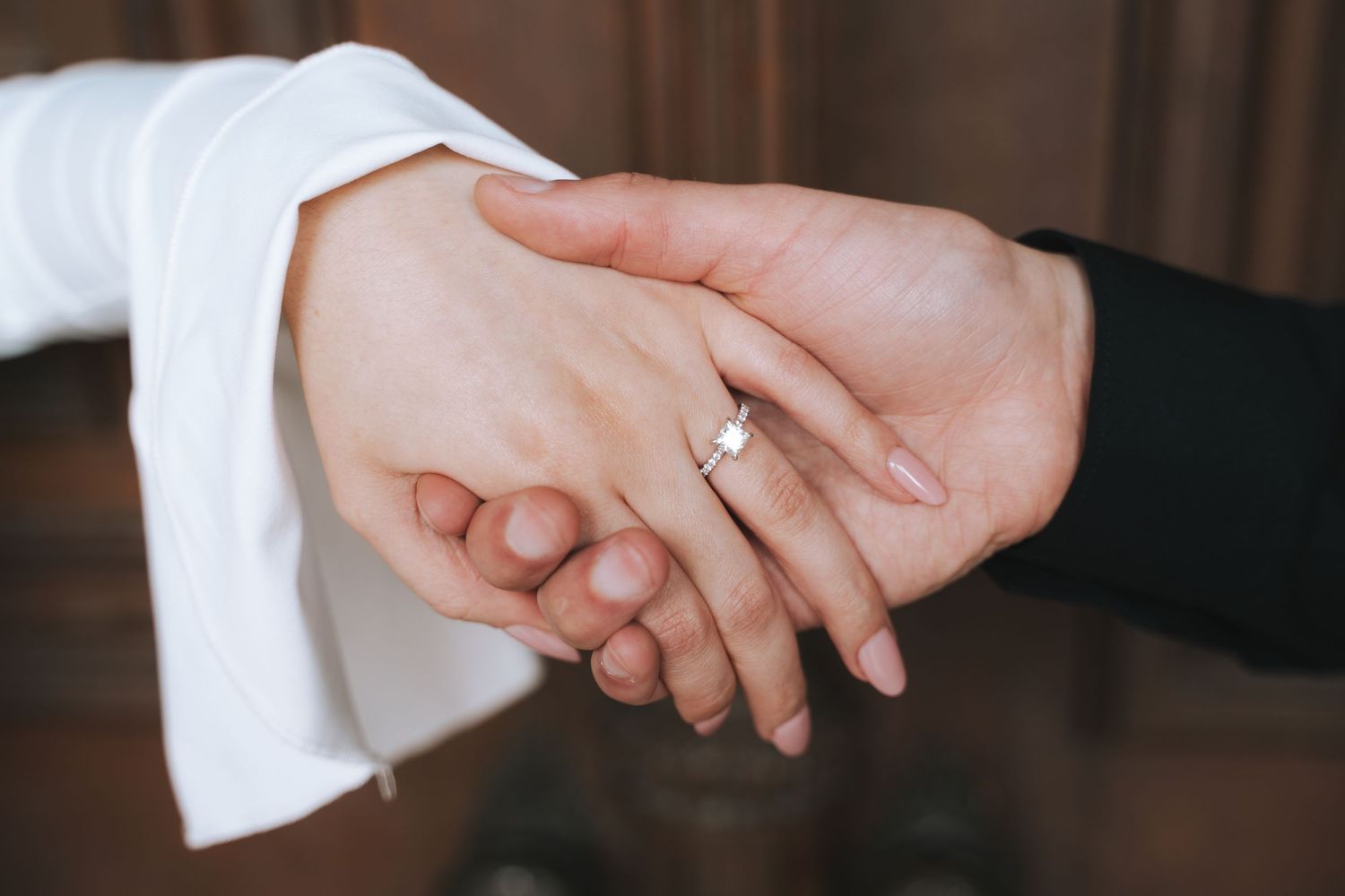 Close-up of intertwined hands showing off a delicate engagement ring.