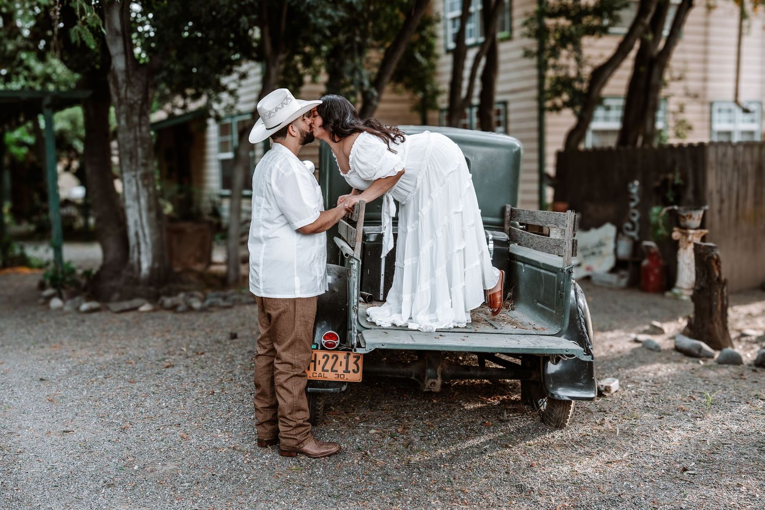 Couple in vintage wedding attire posing beside a classic antique truck outdoors.