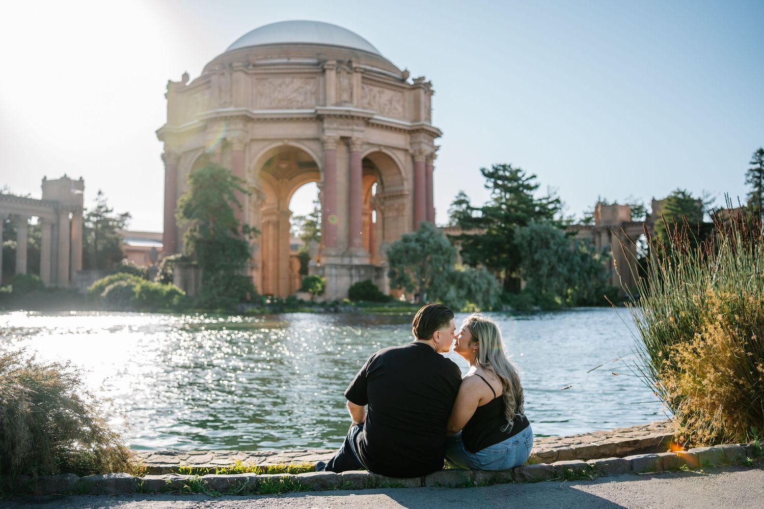 Couple sitting by a lagoon with the Palace of Fine Arts rotunda in San Francisco on a sunny day.