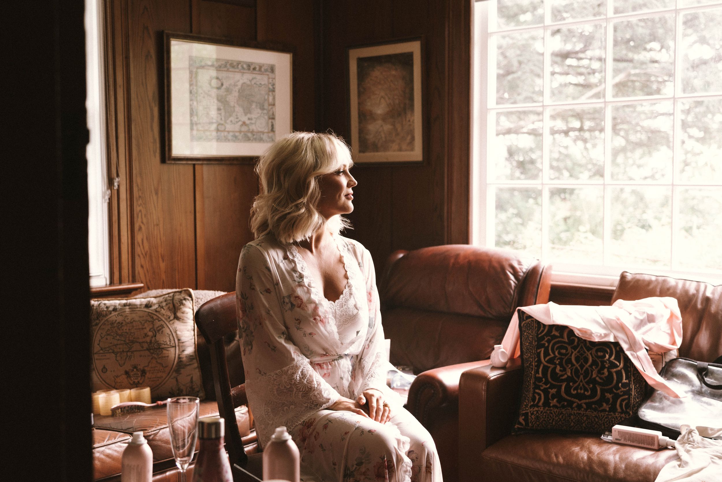 Woman in lace dress sits thoughtfully by window in vintage room.