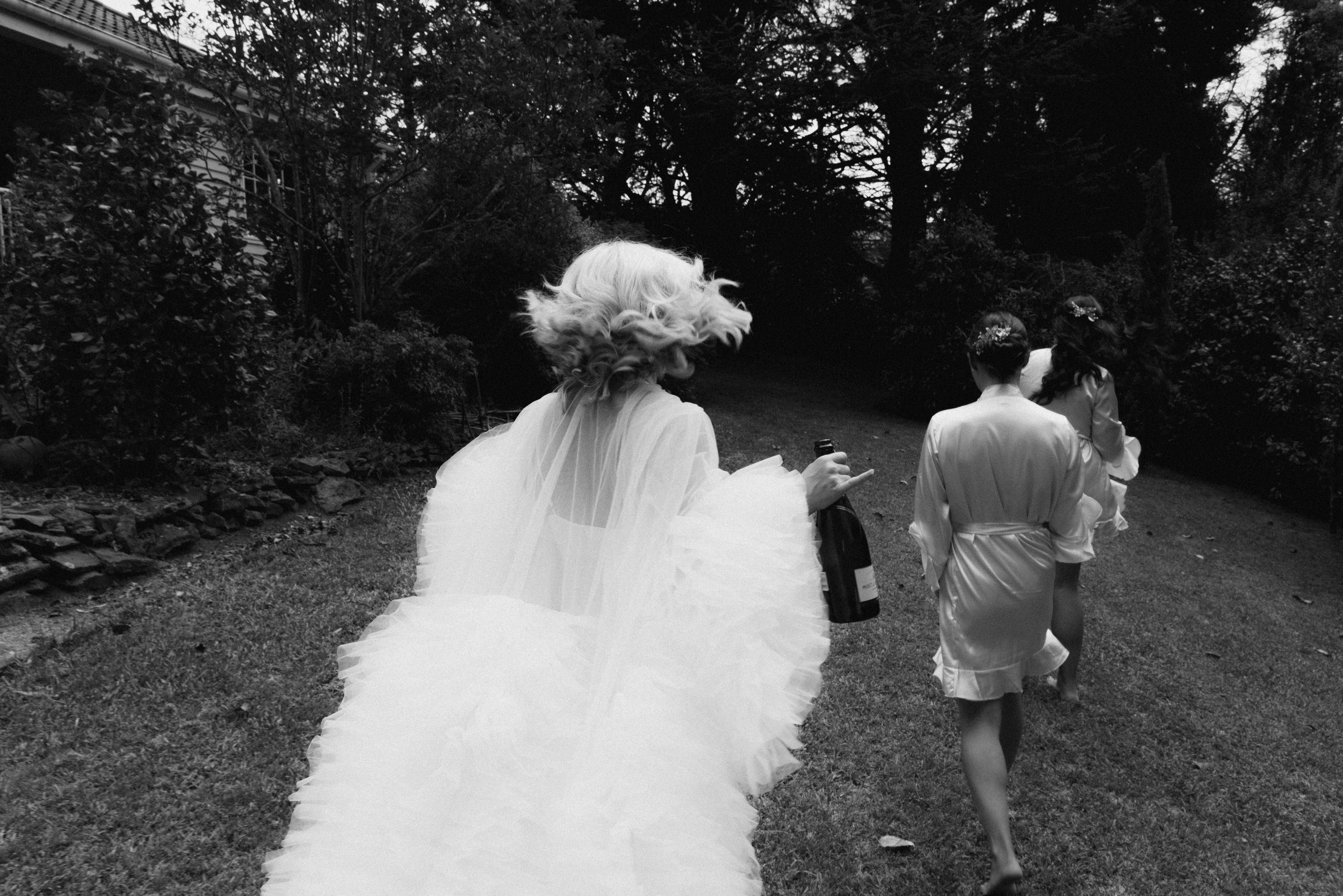 Wedding party walks down garden path with flowing white dress in foreground.
