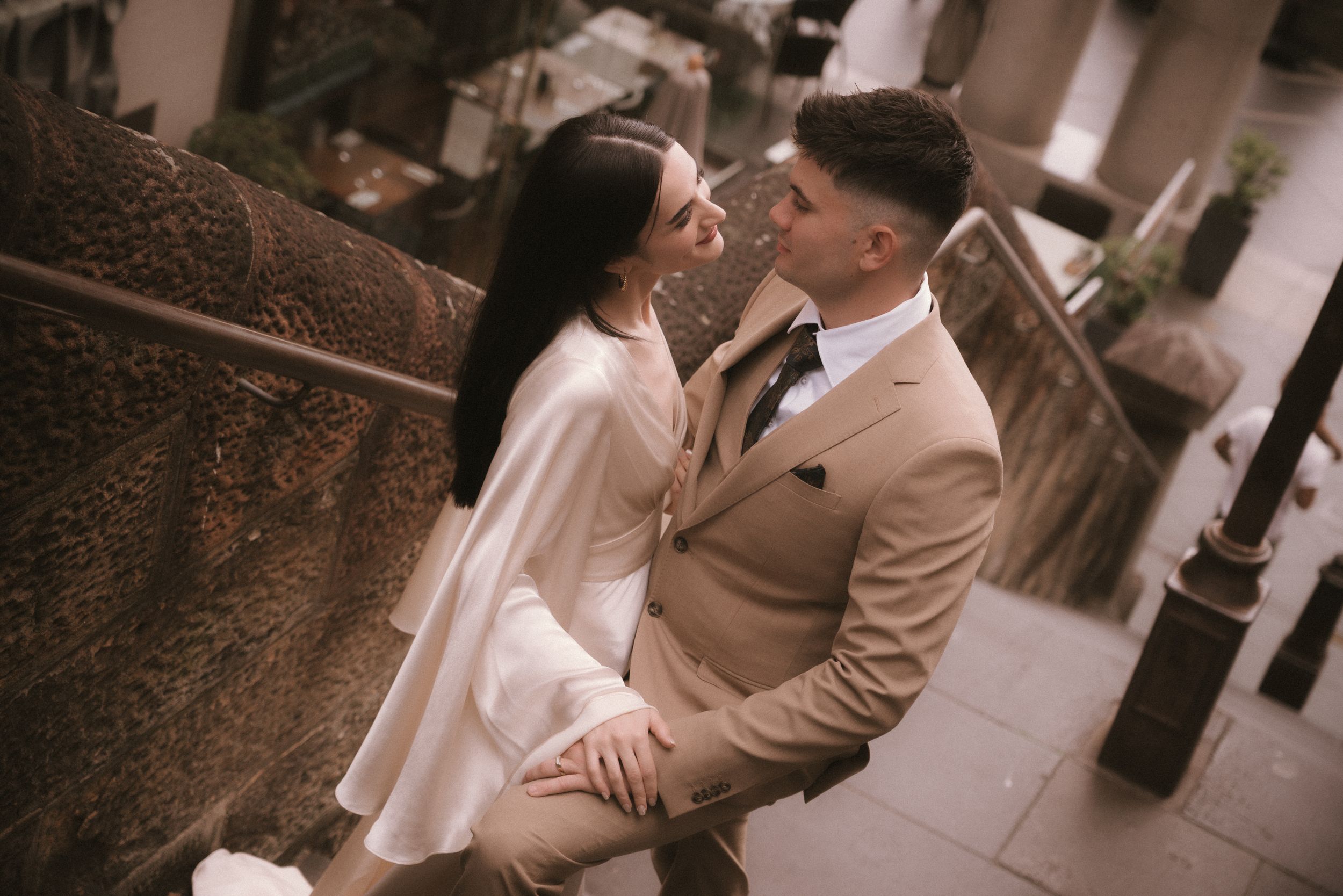 Couple shares intimate moment on stone steps in vintage-toned engagement photo.