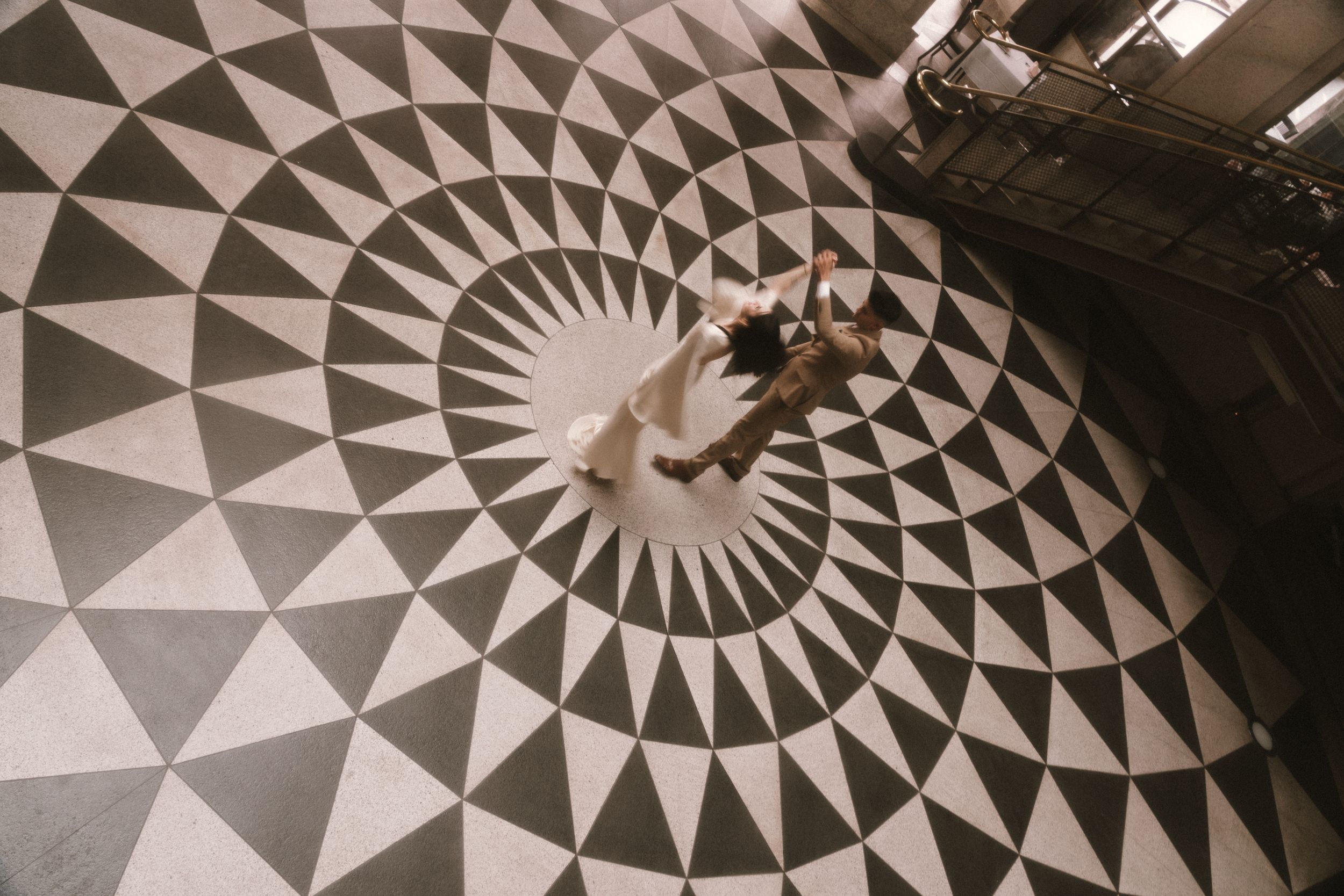 A couple dances on an ornate geometric black and white tiled floor with a striking circular starburst pattern.