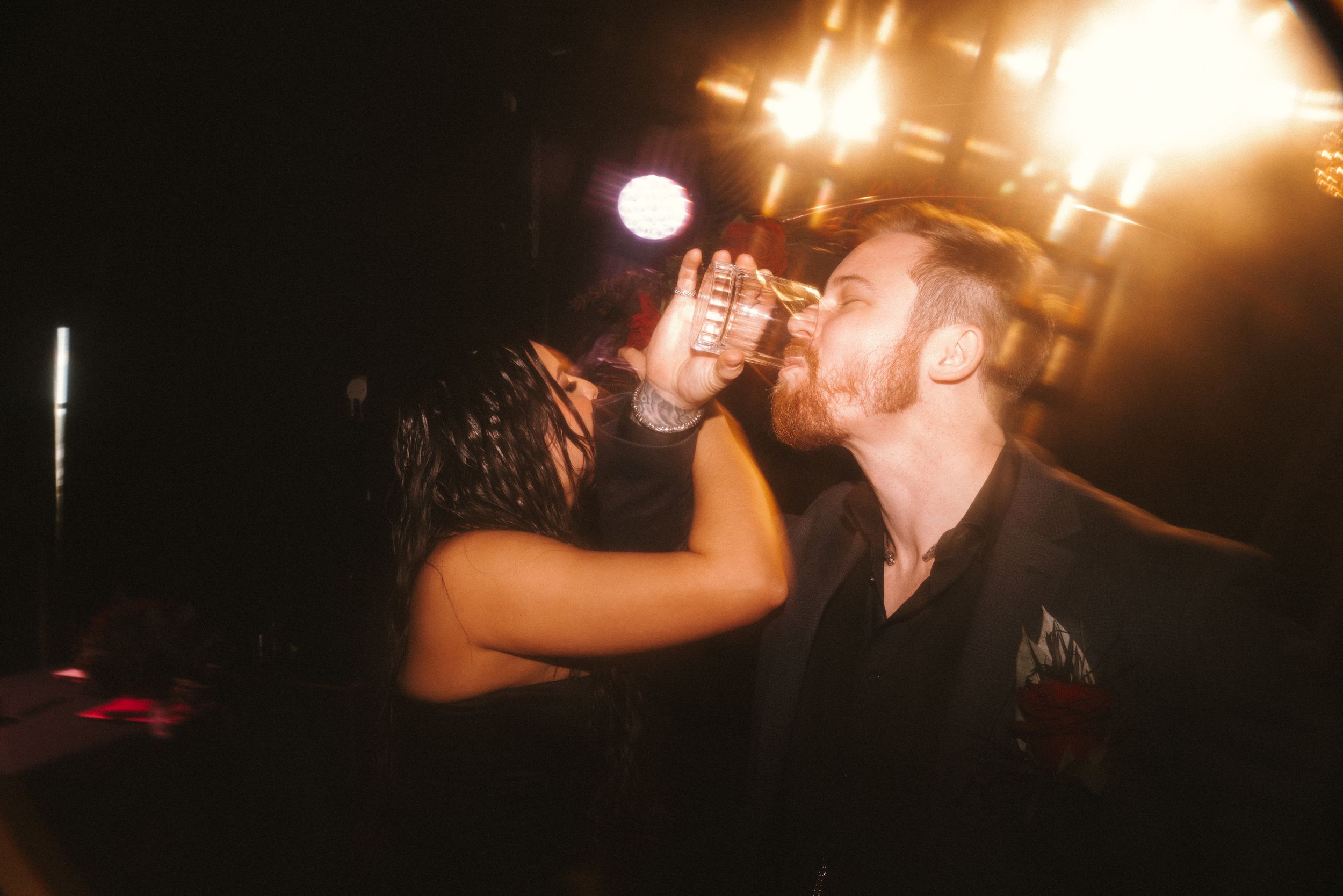 Couple sharing an intimate moment at a dimly lit party with warm glowing lights in the background.