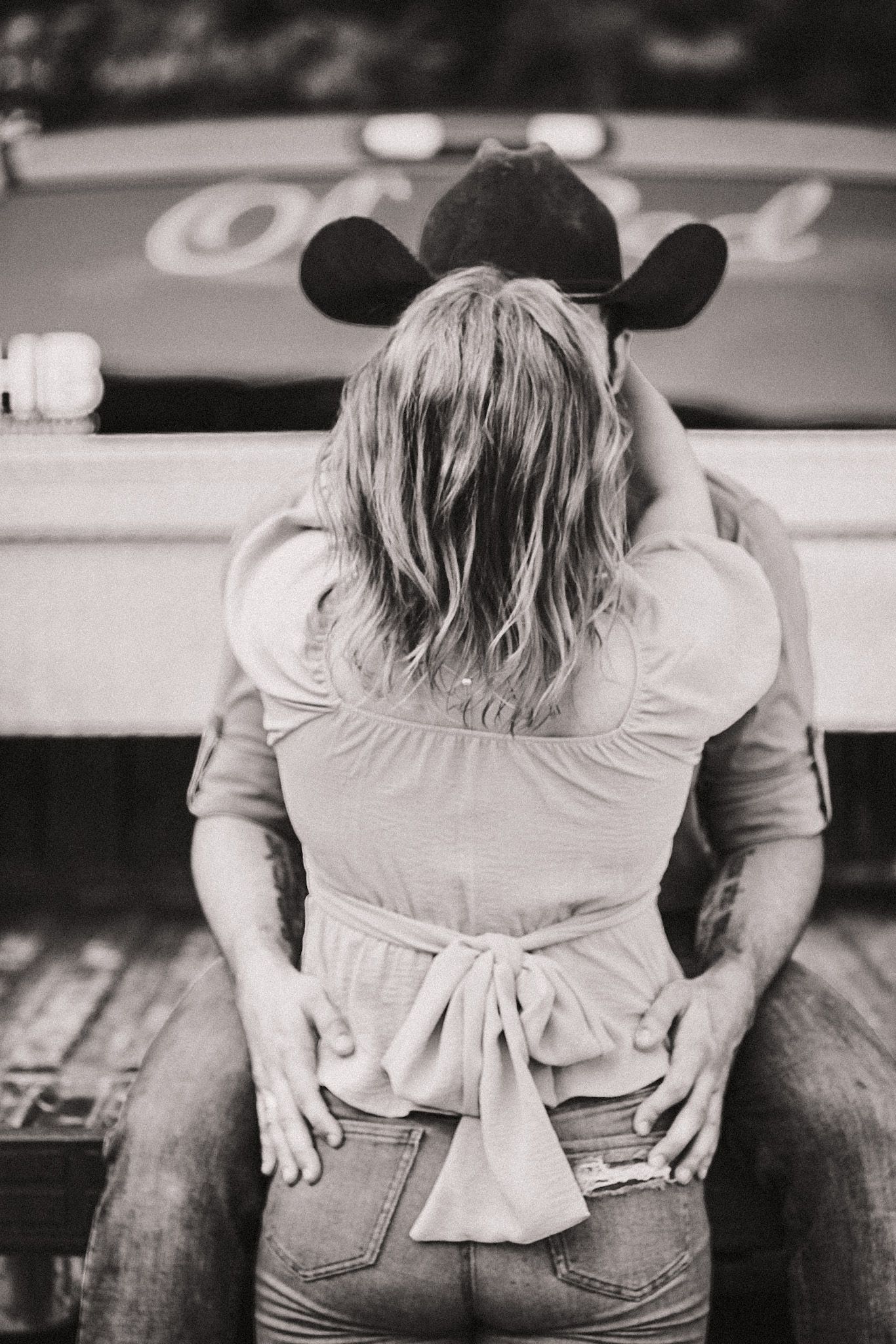 A black and white candid image of a couple facing each other at the back of a pickup truck. Tailgate date photoshoot.