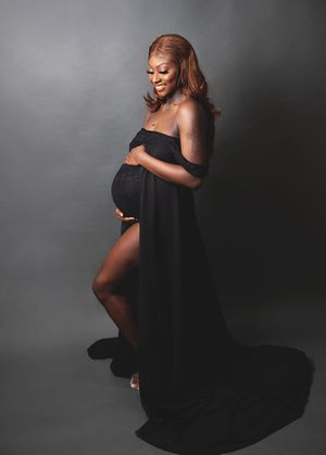 Beautiful maternity portrait featuring pregnant woman in flowing black dress against dark grey background. during a photoshoot in Bexley