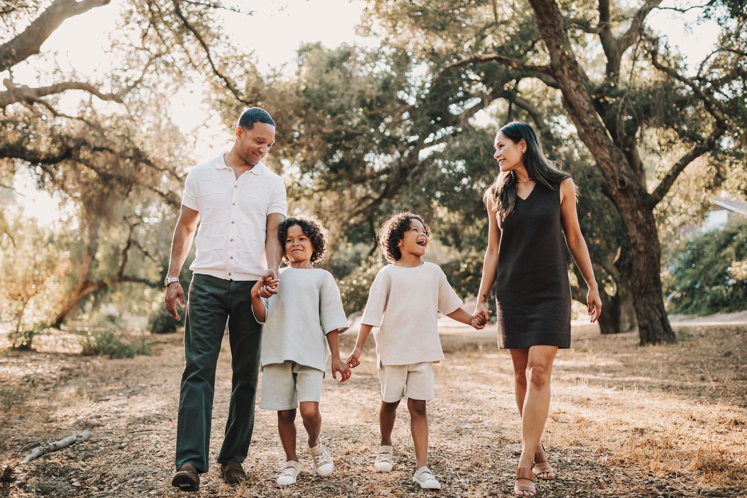 A young family sits together in autumn leaves during an outdoor photo session.