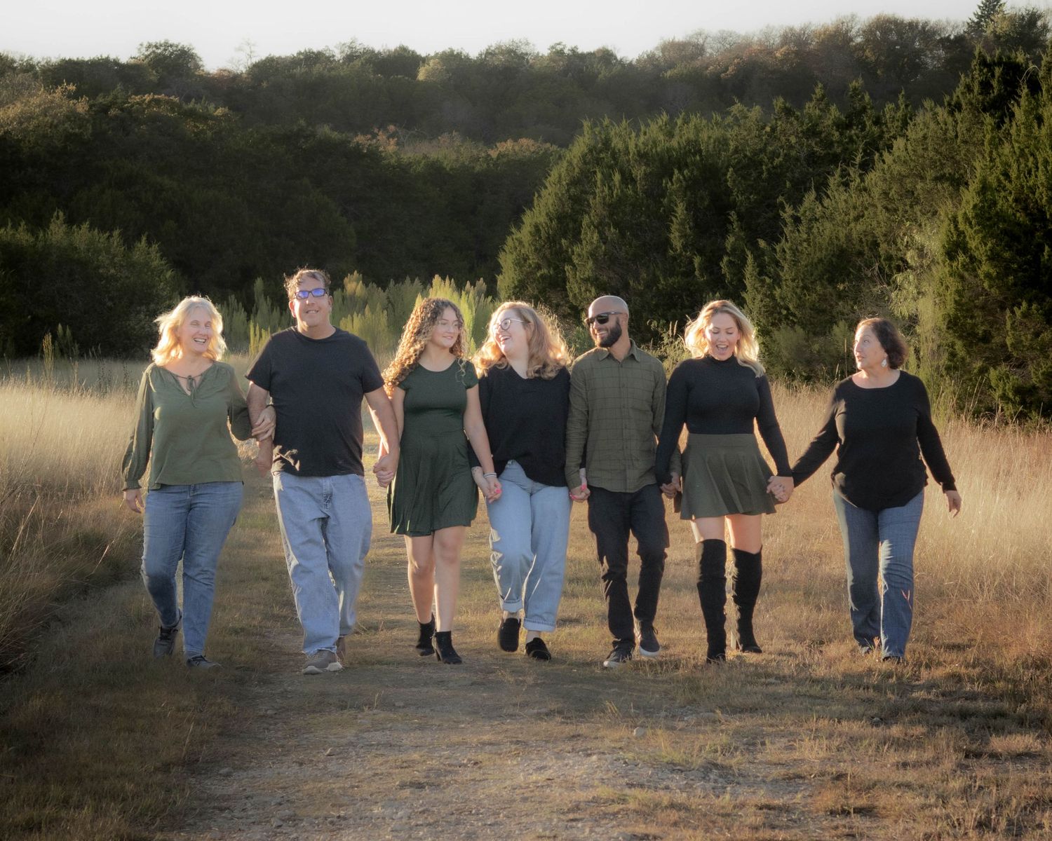 Group of friends walking together on a dirt path at sunset holding hands.